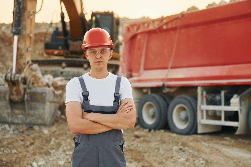 In front of vehicle. Worker in professional uniform is on the borrow pit at daytime